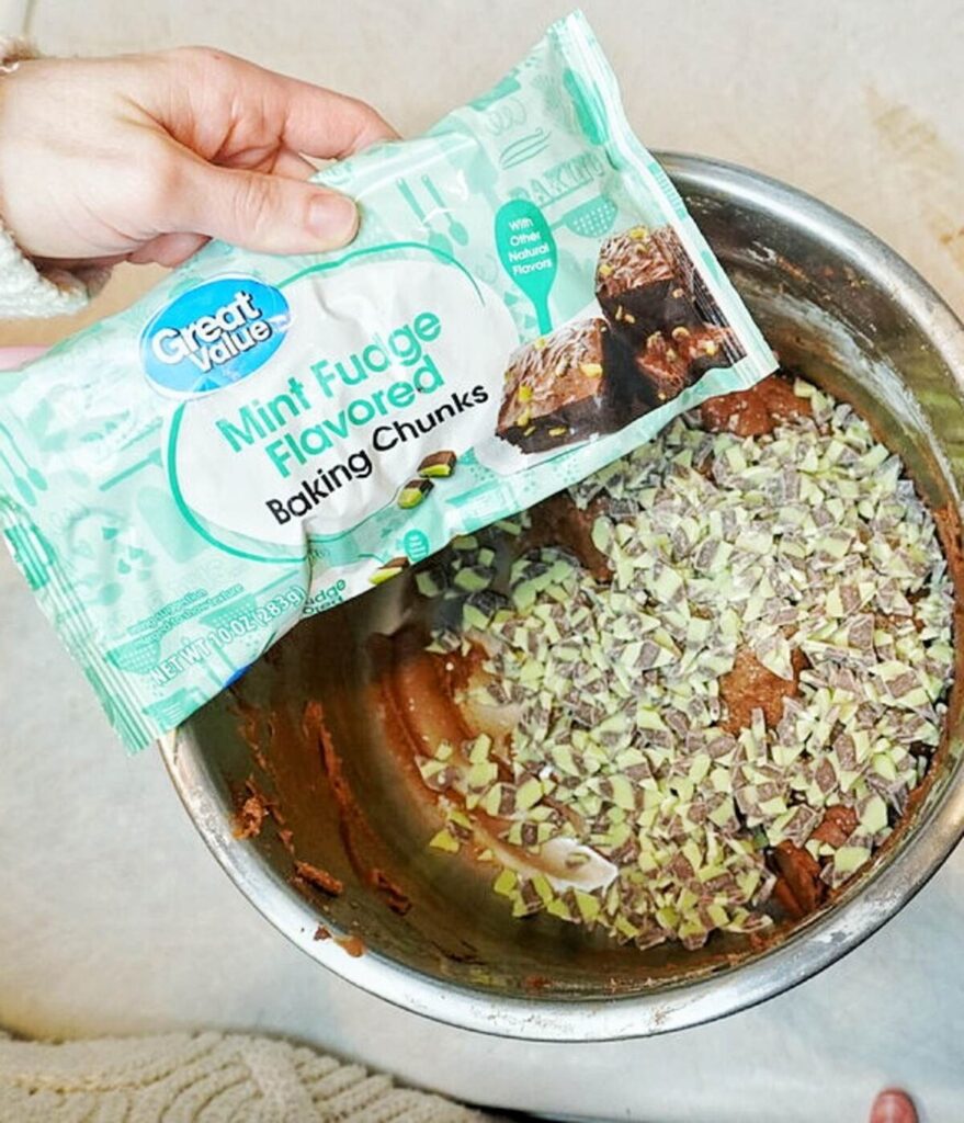 woman holding bag on mint chocolate chip pieces over bowl of cookie dough