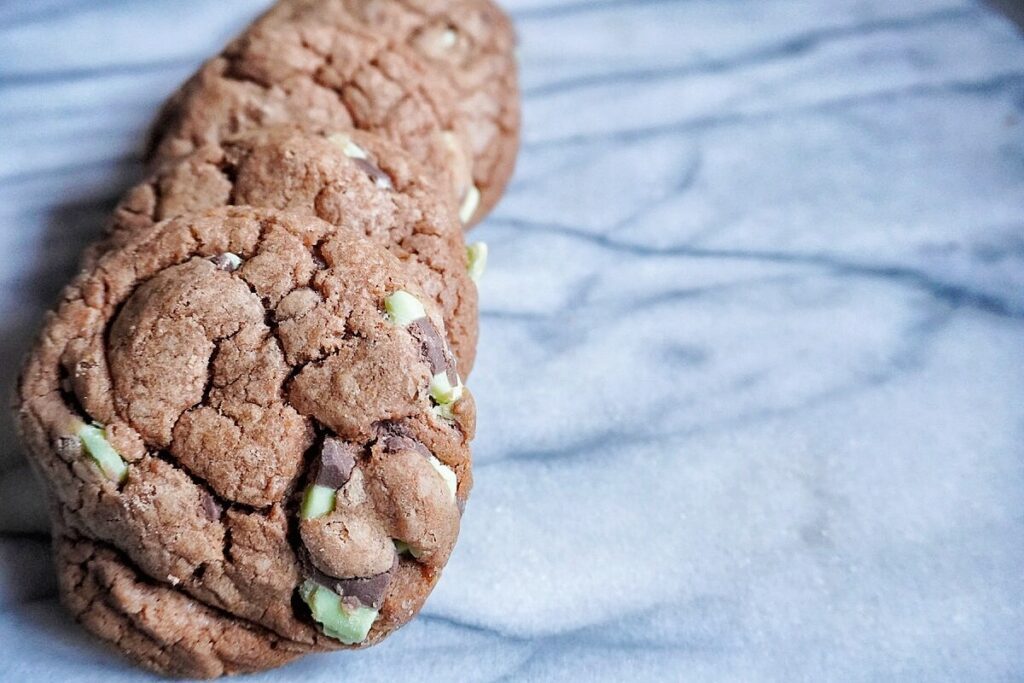 multiple chocolate mint chip cookies lined up in a straight line on a marble tray.