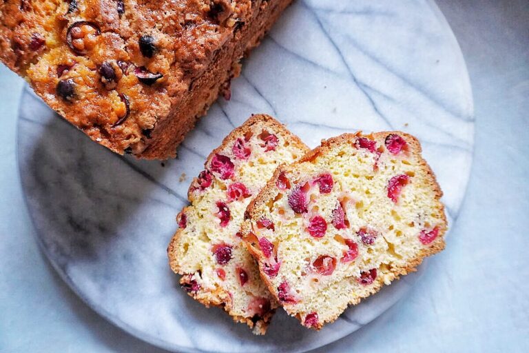 cranberry orange bread loaf on a counter with 2 sliced of bread next to it.