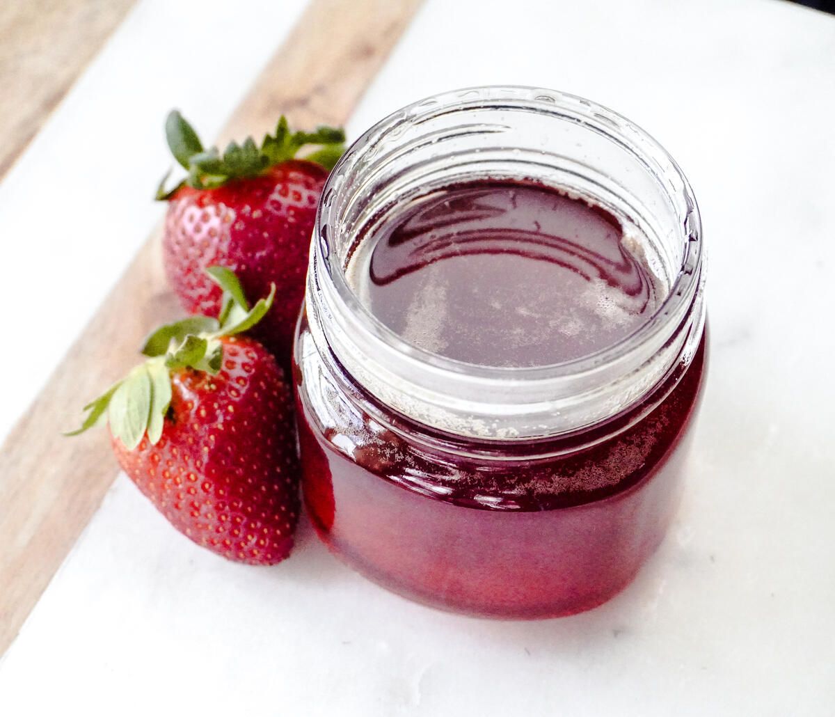 top view looking into jar of strawberry top simple syrup on marble counter with 2 fresh strawberries next to the 1/2 pint jar.