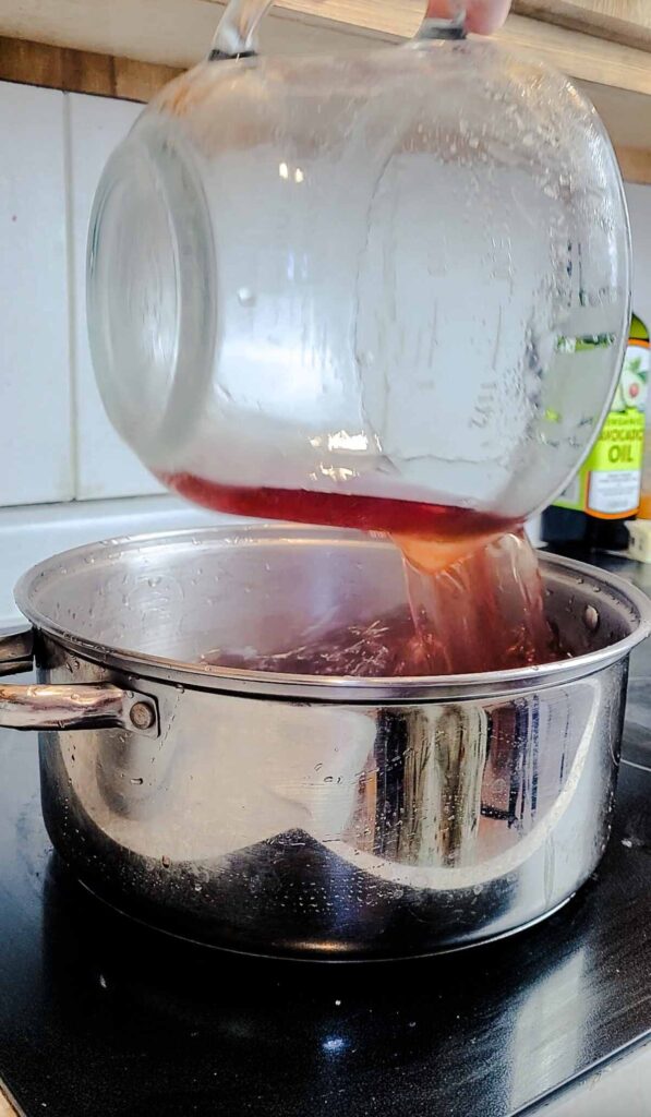 woman pouring infused strawberry juice in to pot on stove top 