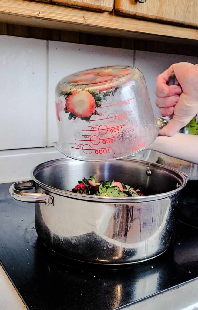 woman pouring strawberry tops into a pot