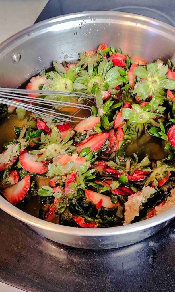 strawberry tops in pot covered in water and being whisked. 