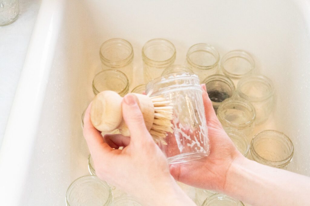 woman washing 1/2 pint canning jars in white sink with soap and scrub brush