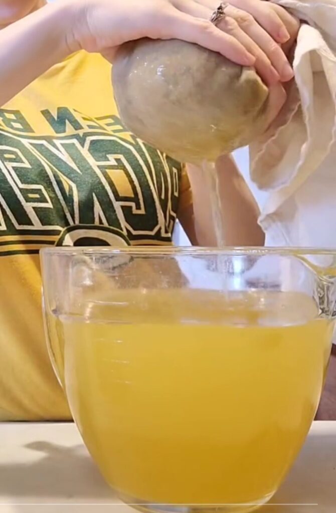 woman straining dandelion tea into glass cup measure.