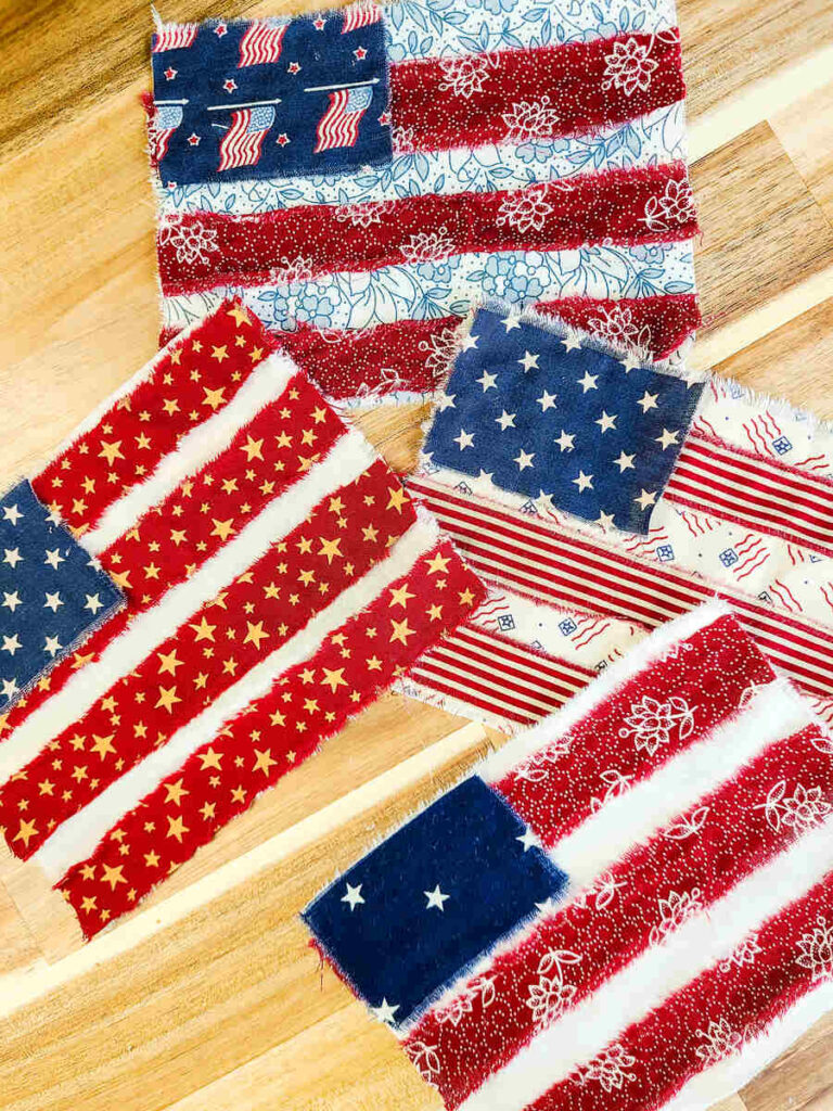 four bunting flags sitting in a row on a wood counter top. They have multiple different fabrics prints of red white and blue. 
