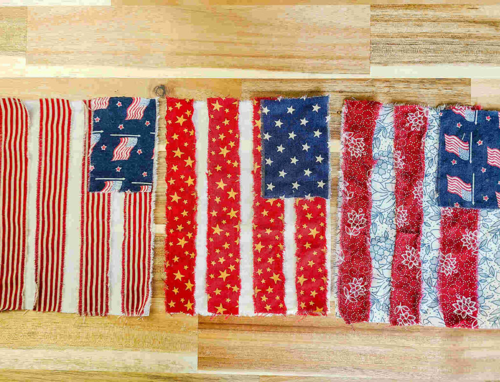 three bunting flags sitting in a row on a wood counter top. They have multiple different fabrics prints of red white and blue. 