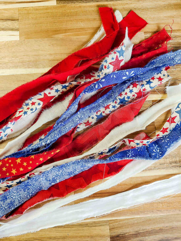 multiple strips of various patriotic color and print fabric on a wood counter top. 