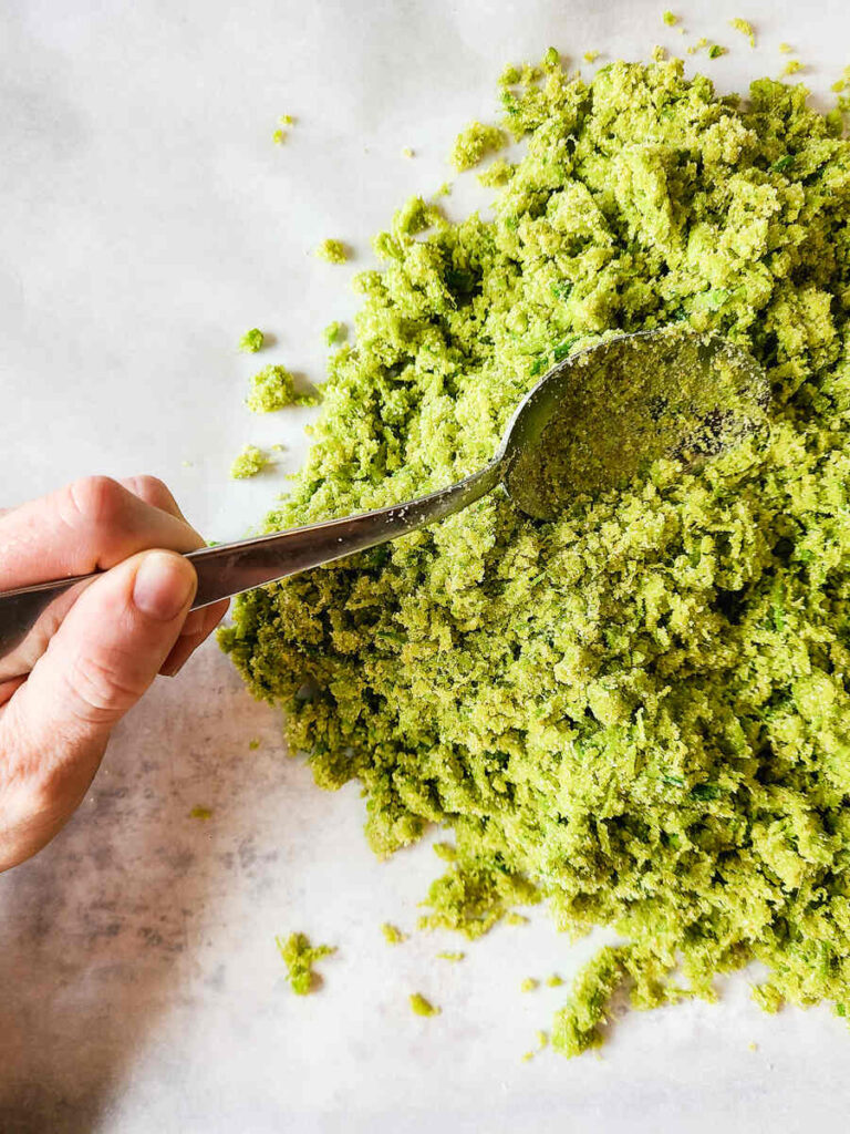 woman spreading garlic scape salt on parchment paper lined cookie sheet