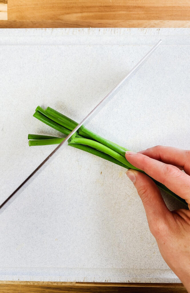 woman cutting garlic scapes with large knife