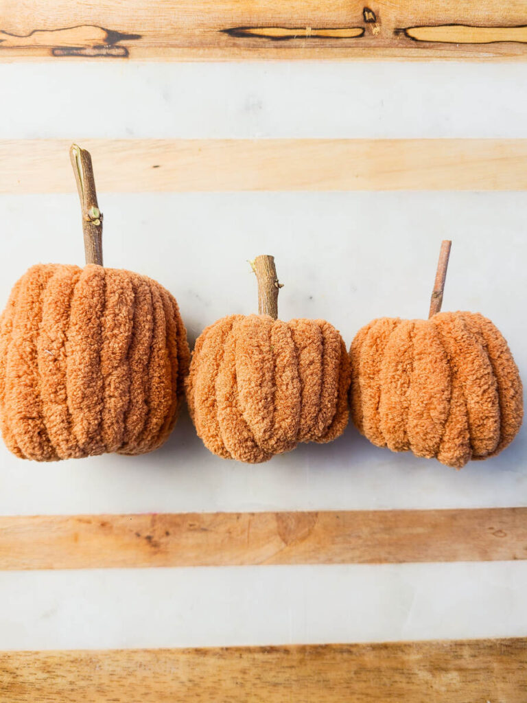 three dark orange yarn pumpkins laid across a marble background in a horizontal row. 