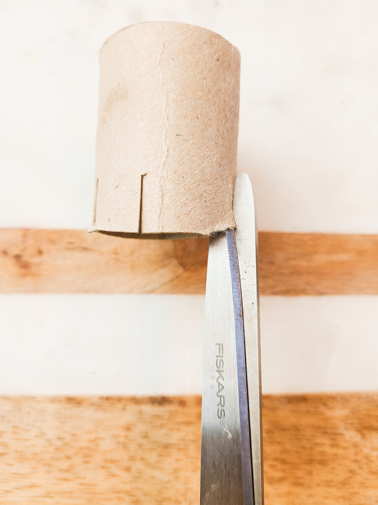 woman cutting small slits vertically in both ends of a toilet paper roll