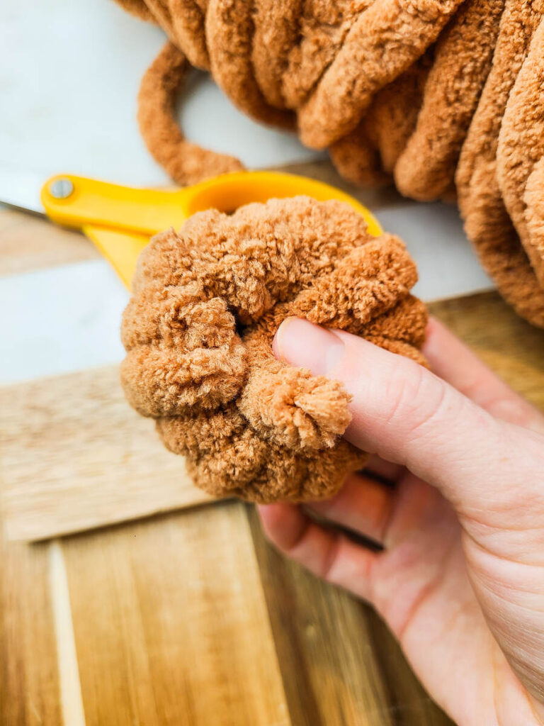woman tucking end of yarn into  center of plush yarn pumpkin 