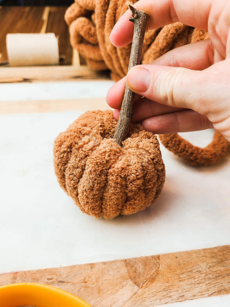 woman inserting stick into center of plush yarn pumpkin 