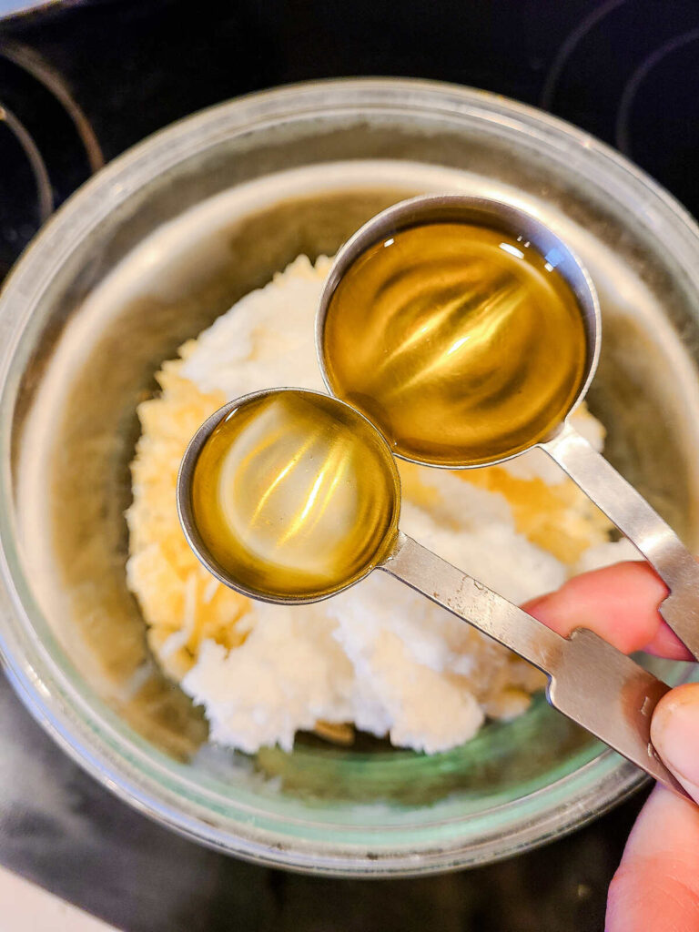 woman holding a tablespoon measurement of oil over a stainless steel pot