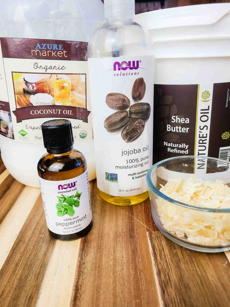 coconut oil, jojoba oil, shea butter, peppermint essential oil, and beeswax all lined up on a counter top for this recipe. 
