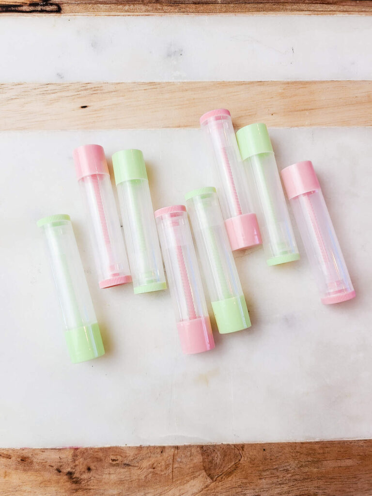 green and pink lip balm tubes lying on marble counter top.