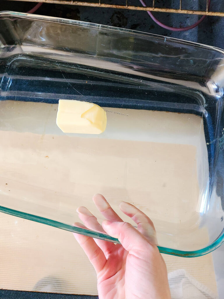 woman putting 13x9" pan with cold butter into preheated oven to melt butter