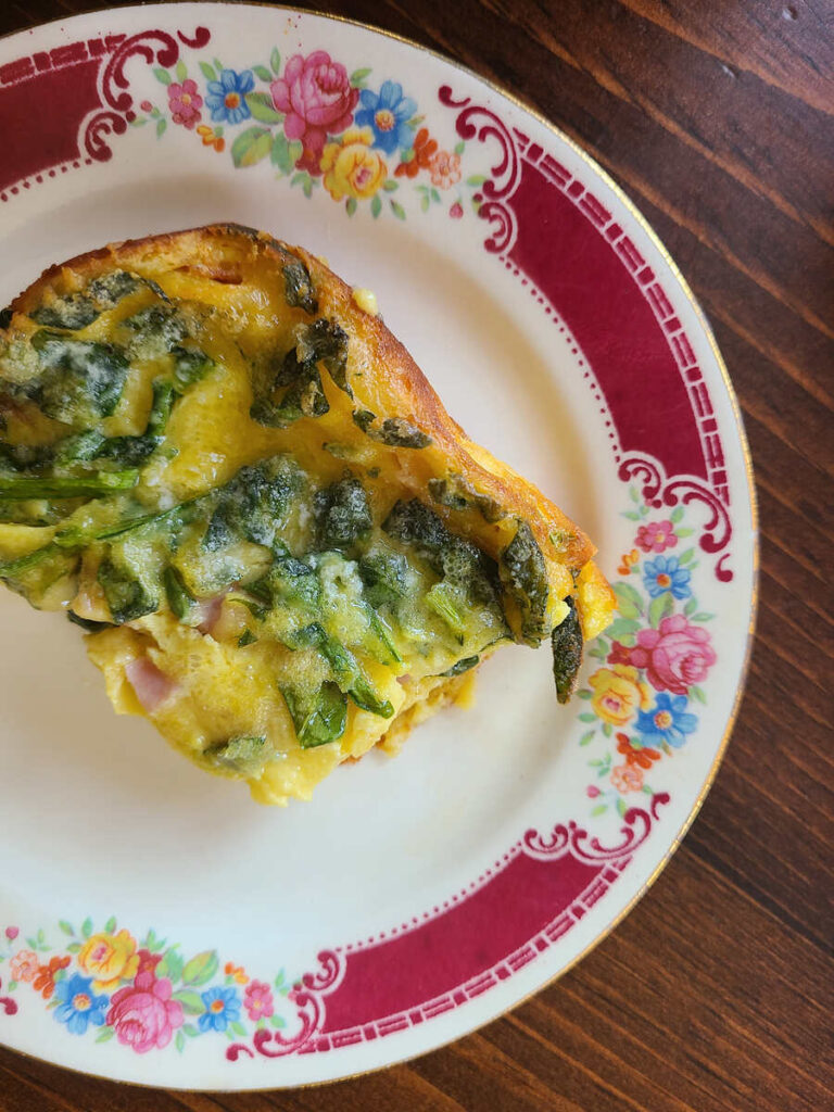 top view of square of German pancake topped with spinach and ham in it on a wood table back drop. 