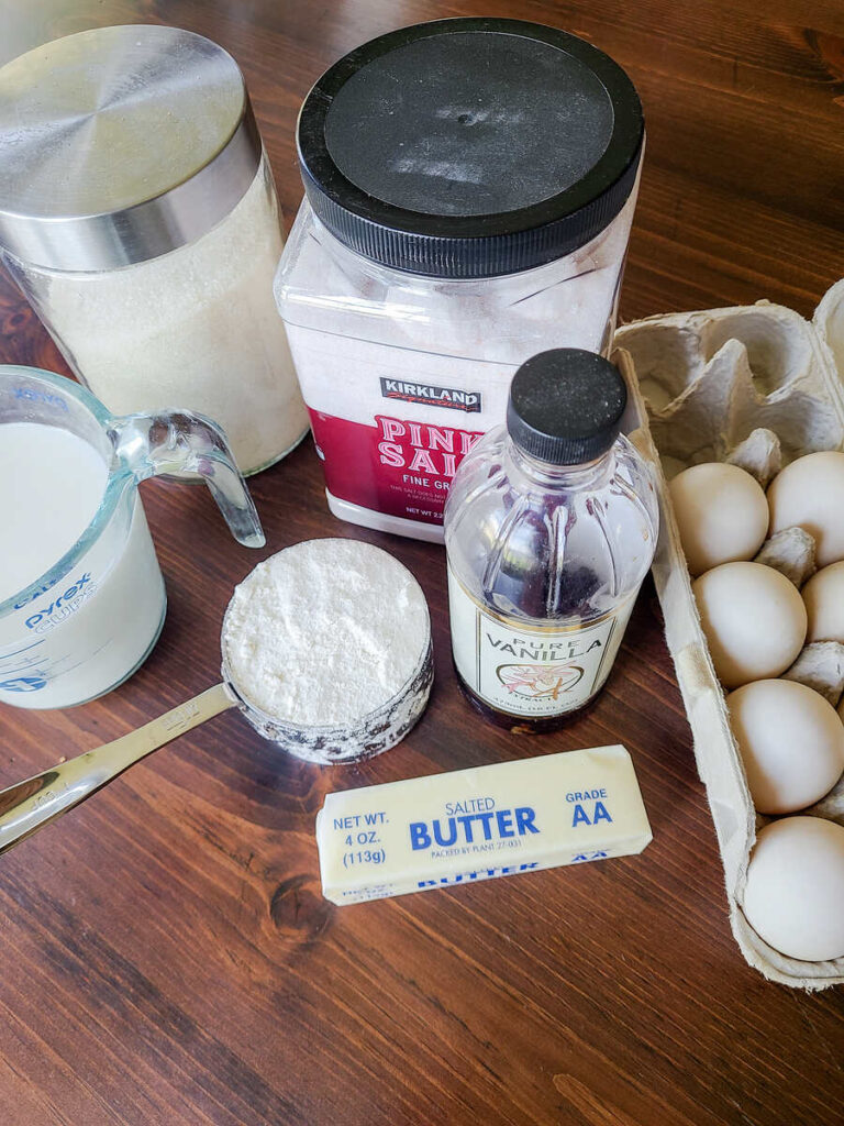 ingredients for German pancakes all set on wood table. eggs, salt, sugar, butter, flour, milk and vanilla 