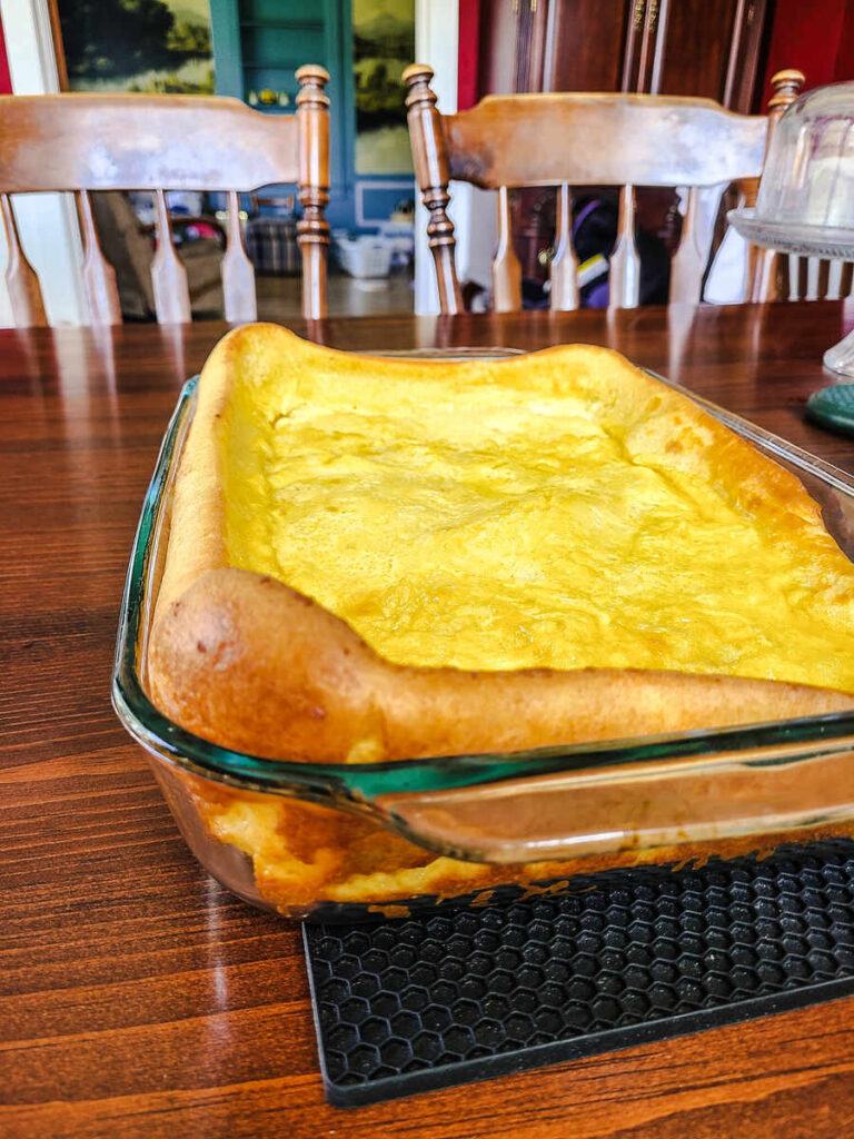 13 x 9 inch pan with a baked German pancake inside cooling on a black hot pad on a dark wood table. 