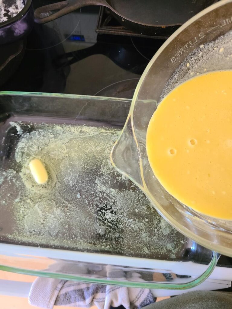 woman pouring German pancake batter into hot pan with melted butter