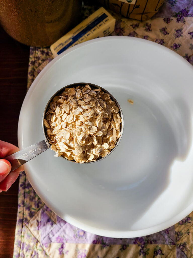 woman measuring oats into white bowl of crust ingredients for rhubarb bars recipe 
