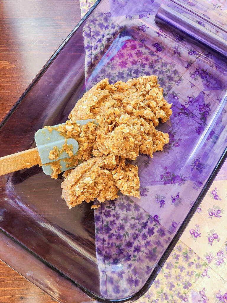 woman spreading oat crumble crust in 13x9"baking dish using a blue silicone spatula 