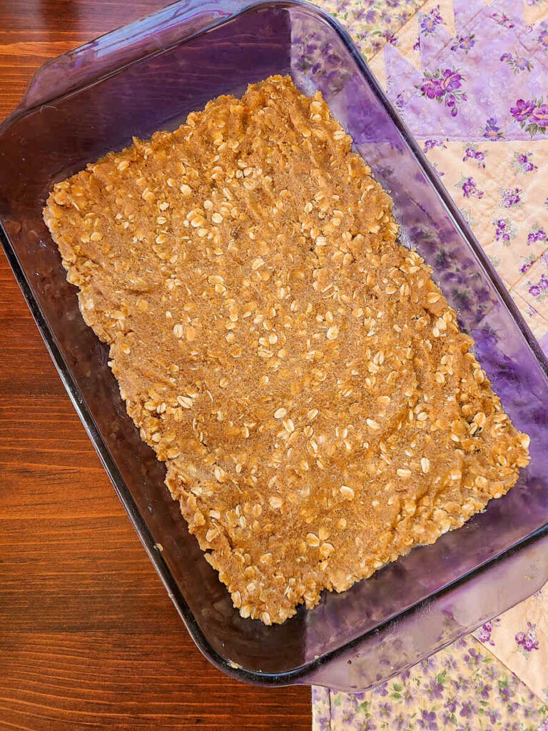 woman spreading oat crumble crust in 13x9"baking dish using a blue silicone spatula 