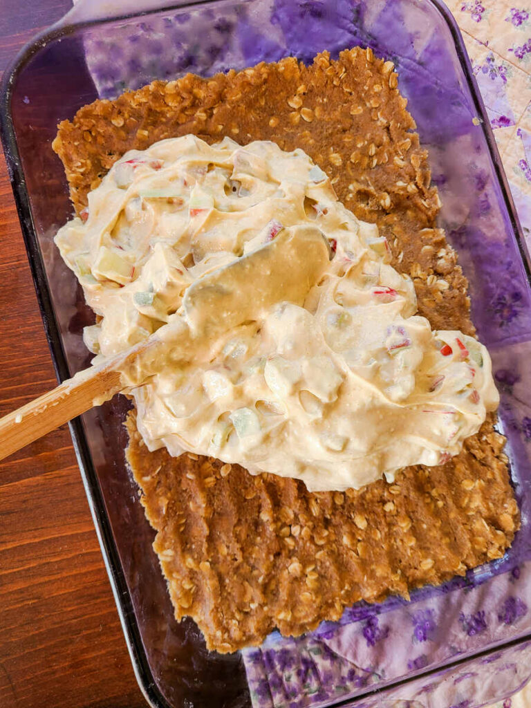 woman spreading cream cheese mixture over crust with spatula 