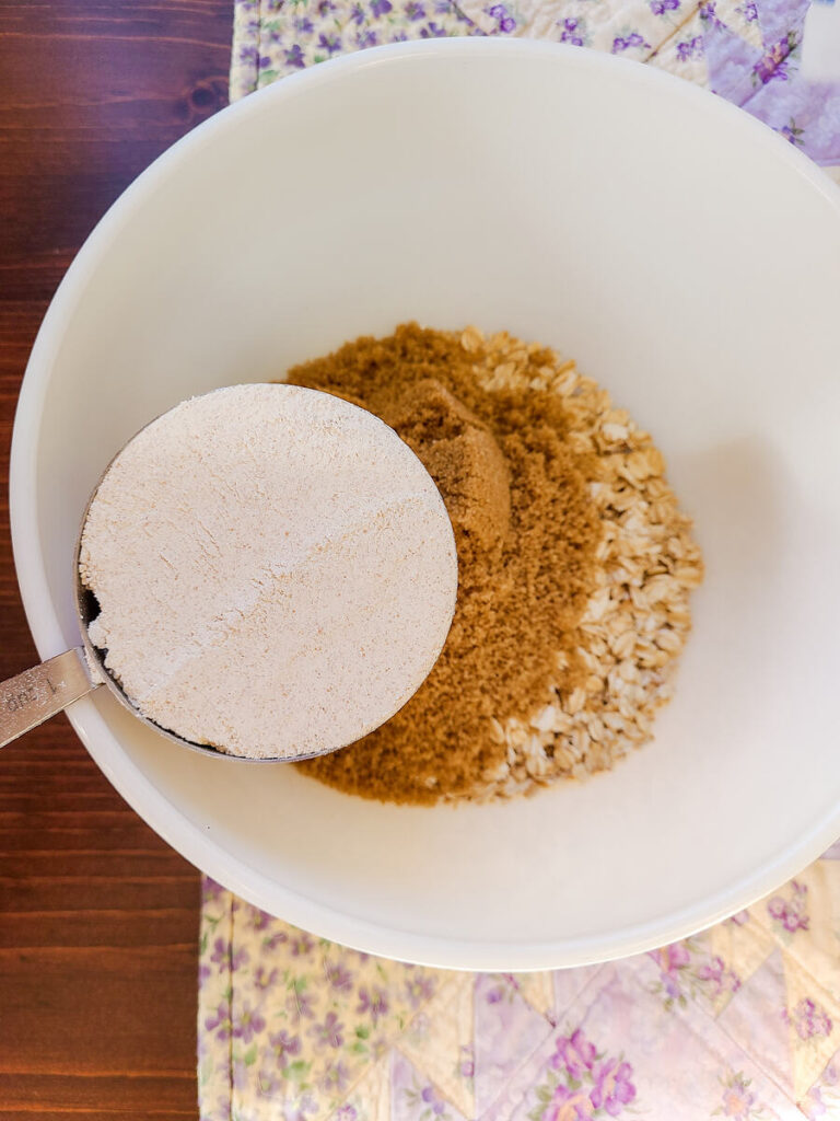 woman pouring cup of fresh einkorn flour into white bowl with other crumble ingredients 