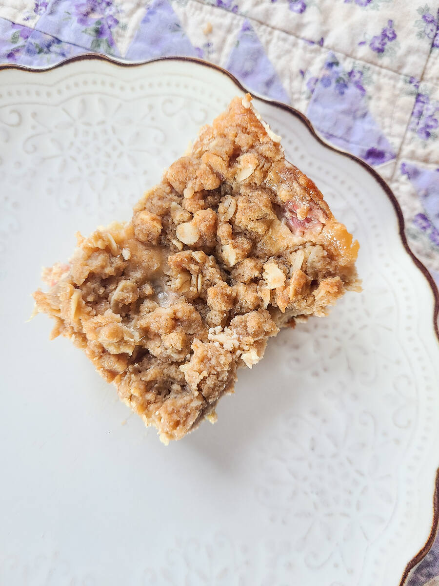 rhubarb crumble cream cheese bar square set on a scalloped white plate with a purple quilt background