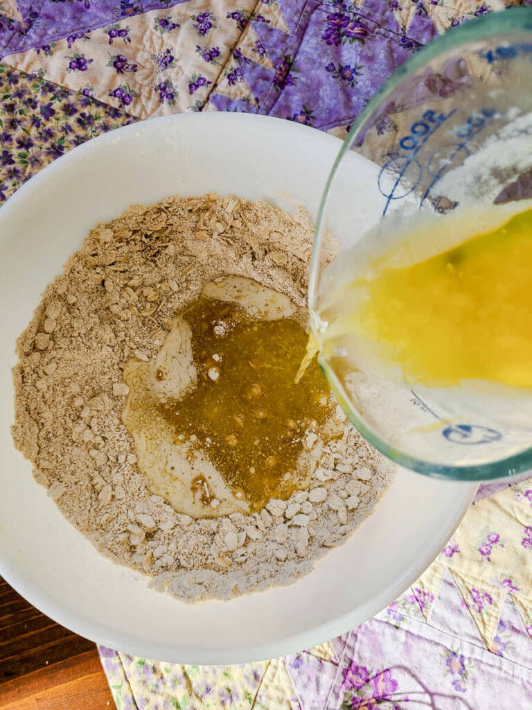 woman pouring melted butter into dry ingredient mixture for crust