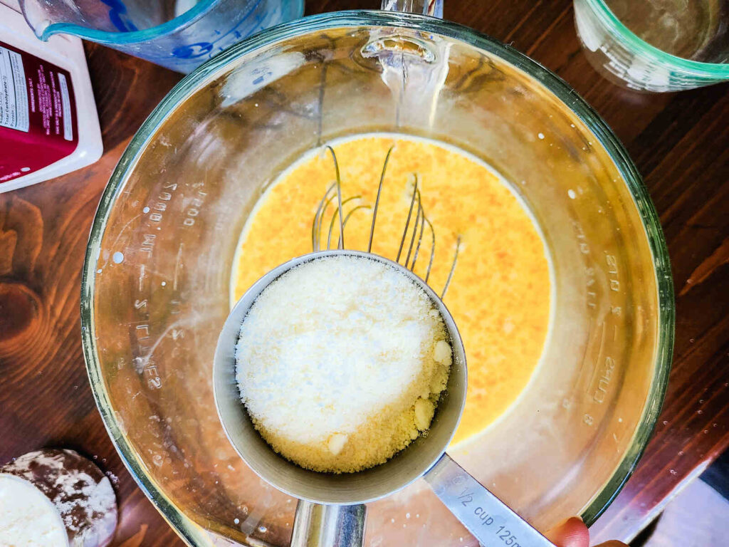 woman pouring parmesan cheese into milk and egg mixture