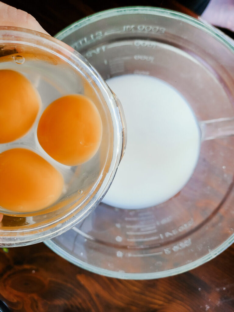 woman pouring cracked eggs into liquid measuring cup of milk