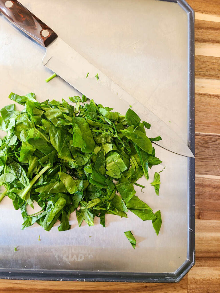 woman chopping spinach on stainless steel cutting board with chef knife 