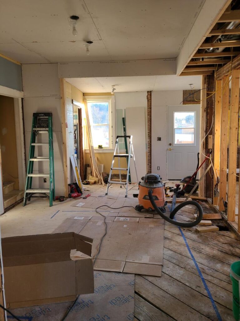 room that has studs showing, no floors or ceiling. ladder and shop vac in the middle of the room , wall taken out to expose window 