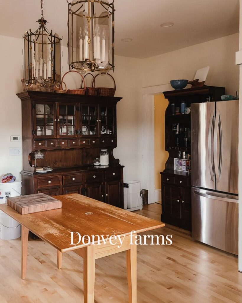picture of a kitchen styled like an unfitted kitchen with 2 hutches, a stainless steel fridge to the right and a table in the center. 