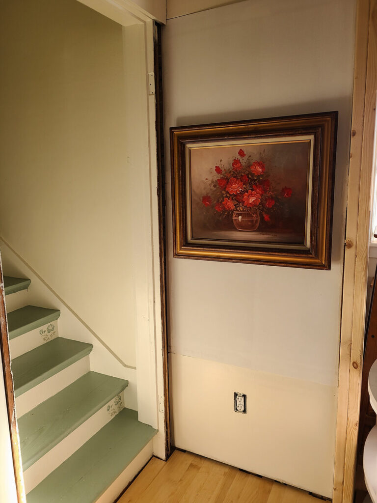 corner with blue and white stairs to the left, white wall with gold framed pink rose painting to the right. 