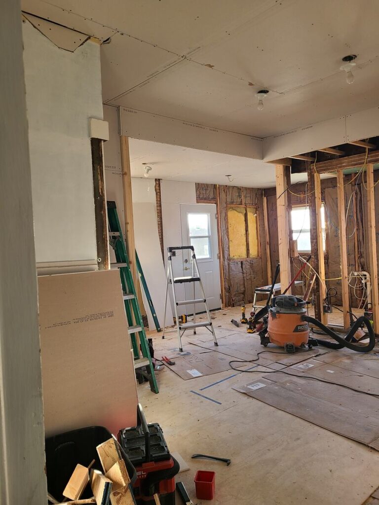 room that has studs showing, no floors or ceiling. ladder and shop vac in the middle of the room 