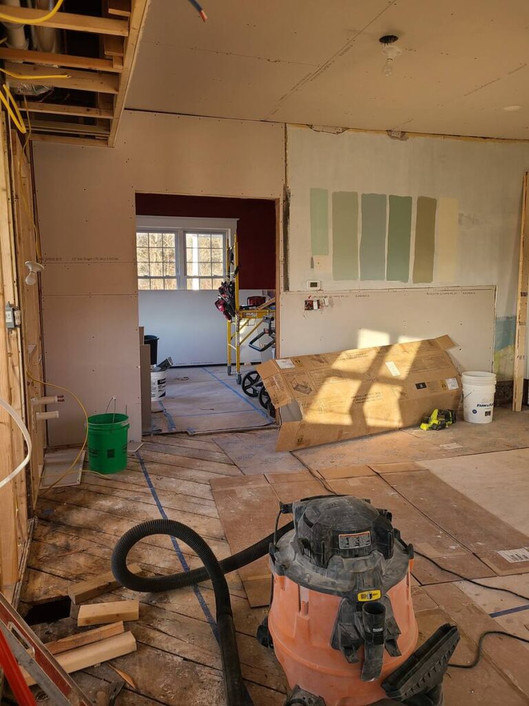 room that has studs showing, no floors or ceiling. ladder and shop vac in the middle of the room , blue paint samples on the wall. 