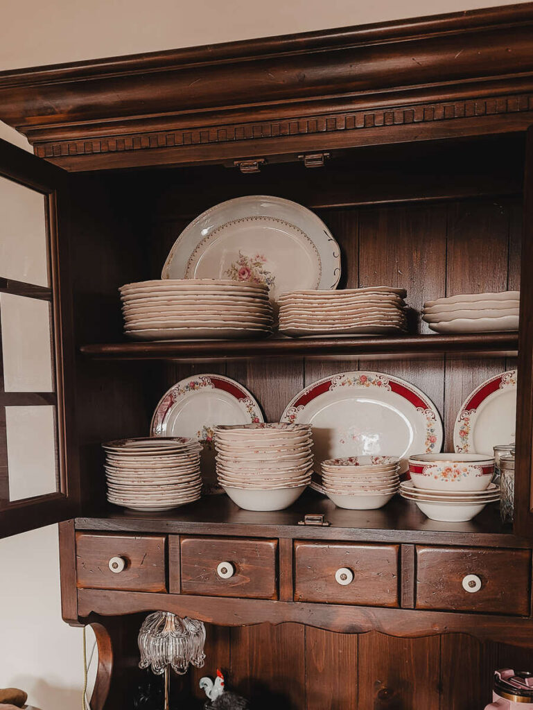 open door of dark wood hutch with pink floral dishes stored inside plates in back bowls in the front 