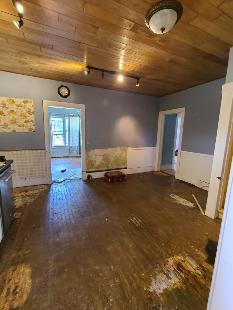 empty dirty kitchen with wood ceiling, blue walls, white trim and wall panels, and a dark wood floor. 