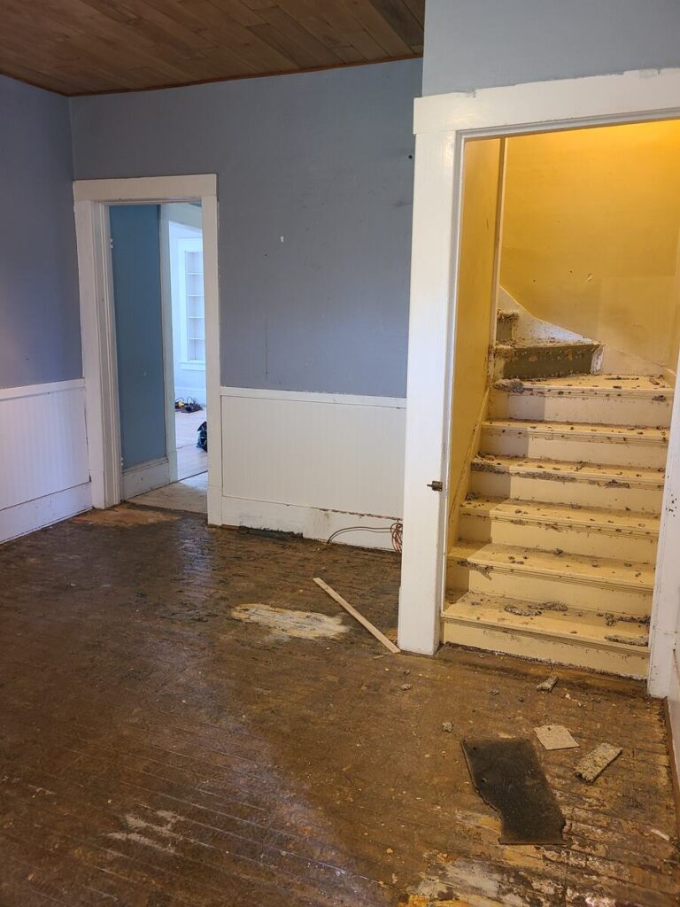 empty dirty kitchen with wood ceiling, blue walls, white trim and wall panels, and a dark wood floor. , stairs with carpet ripped out 