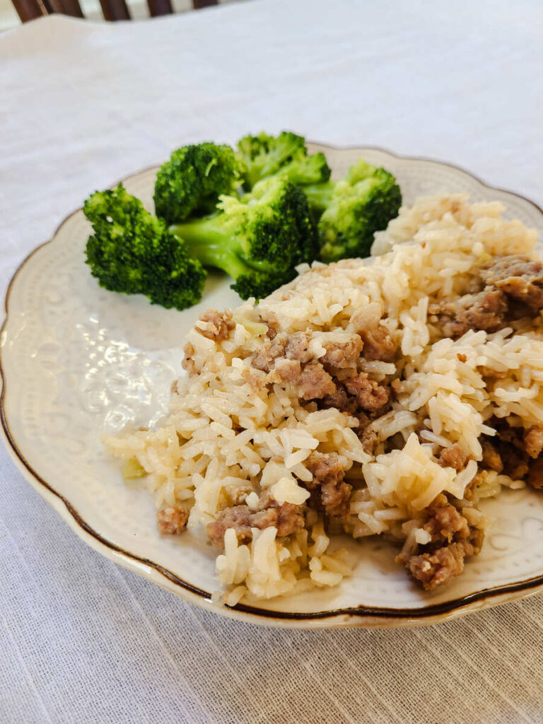 Simple Sausage Rice Dinner Instant Pot and Stovetop Recipe. white tablecloth with cream scalloped dinner plate full of sausage rice with broccoli on the side.