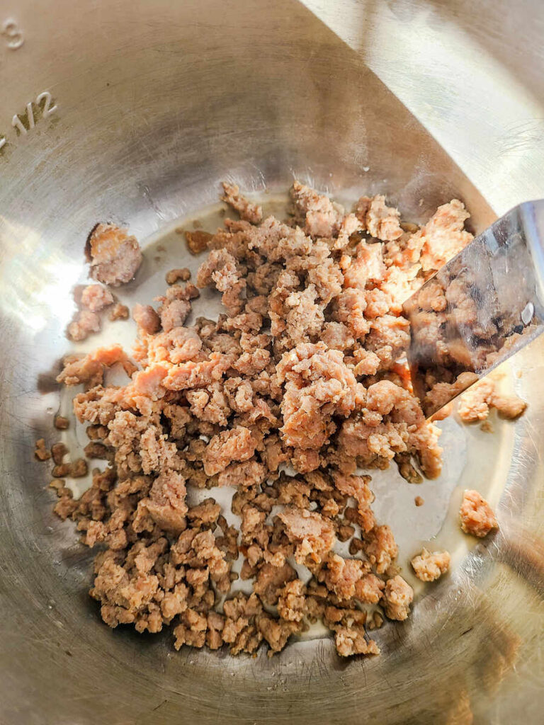 woman sautéing ground sausage in instant pot with metal spatula