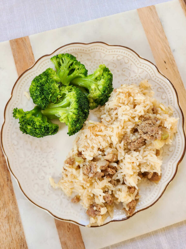 Simple Sausage Rice Dinner Instant Pot and Stovetop Recipe. marble and wood cutting board with cream scalloped dinner plate full of sausage rice with broccoli on the side.
