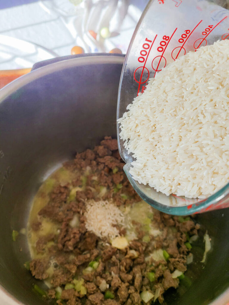 woman adding rice to instant pot to cook in broth mixture