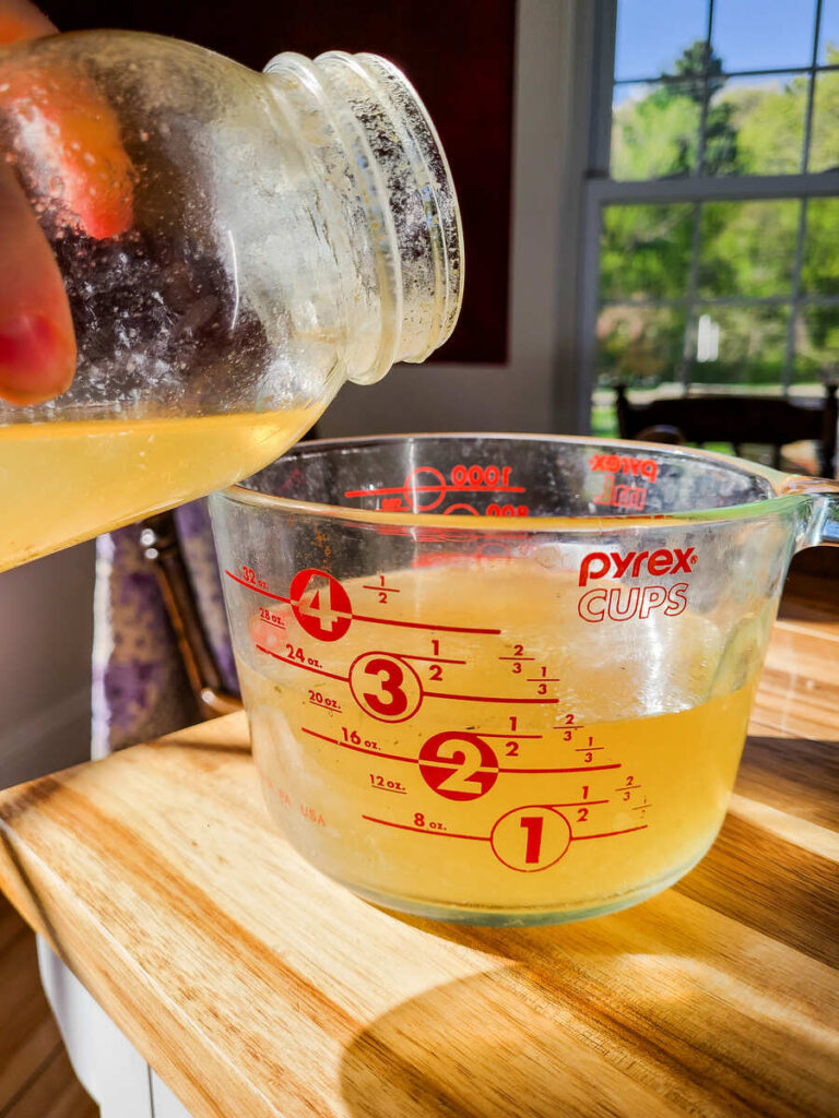 woman pouring liquid chicken broth into liquid measuring cup to add to instant pot of sausage and veggies