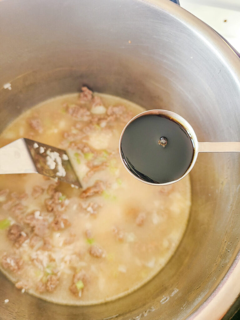 woman adding soy sauce to instant pot broth mixture